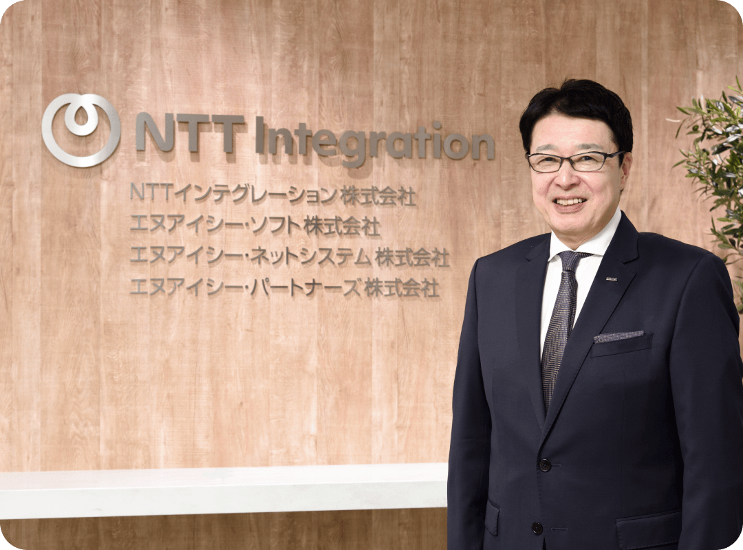 社内にあるエヌアイシー・パートナーズのロゴ看板を背景に写っている須崎吾一代表取締役社長